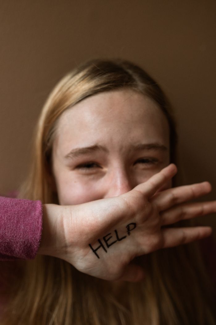 A distressed teenager covering face with 'HELP' written on hand, signifying need for support.